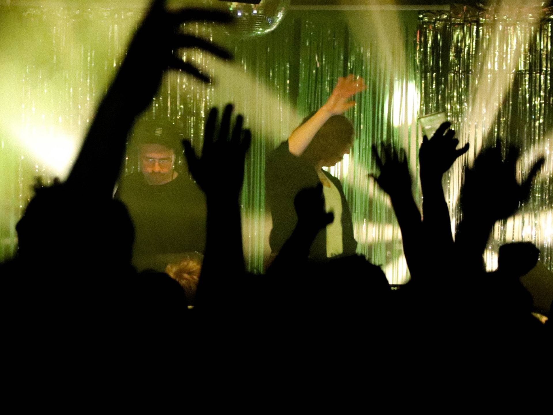 Hands and arms lifted in the air, view looking through them at a stage with yellow lighting