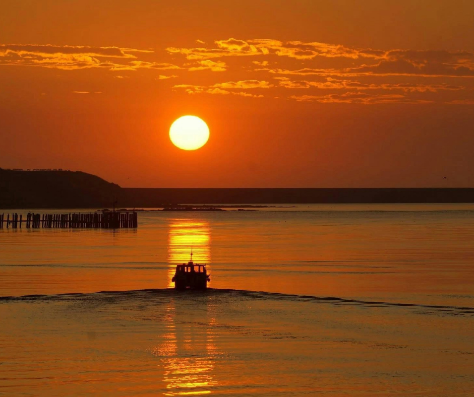 A boat out at sea travelling towards a sunset 