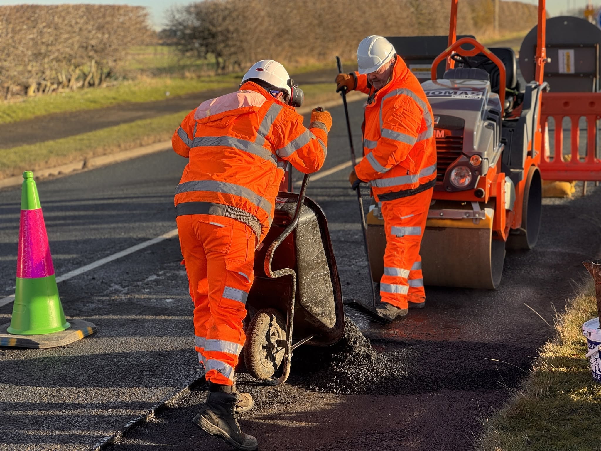 Two people in high-vis clothing laying bitumen onto the road