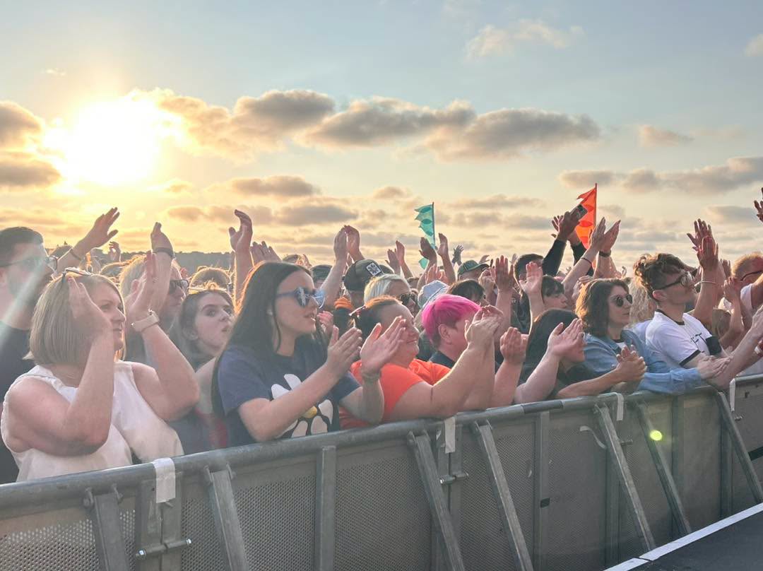 Cheering Crowds in front of the stage, with a beautiful sunset in the back round.