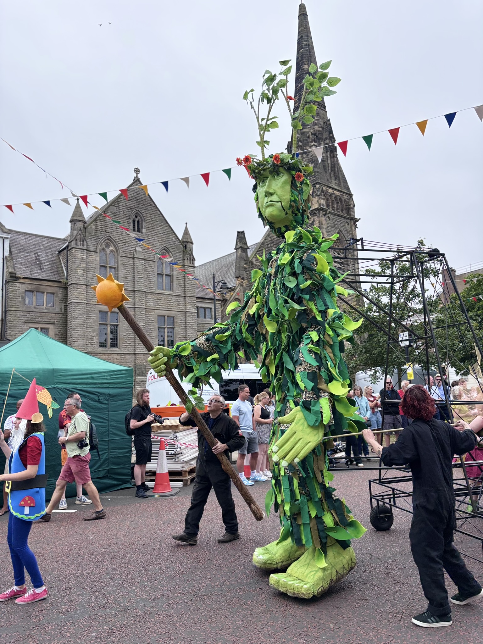 An enormous, green puppet, wanders through the streets of Tynemouth, staff in hand as part of the parade, pre-concert