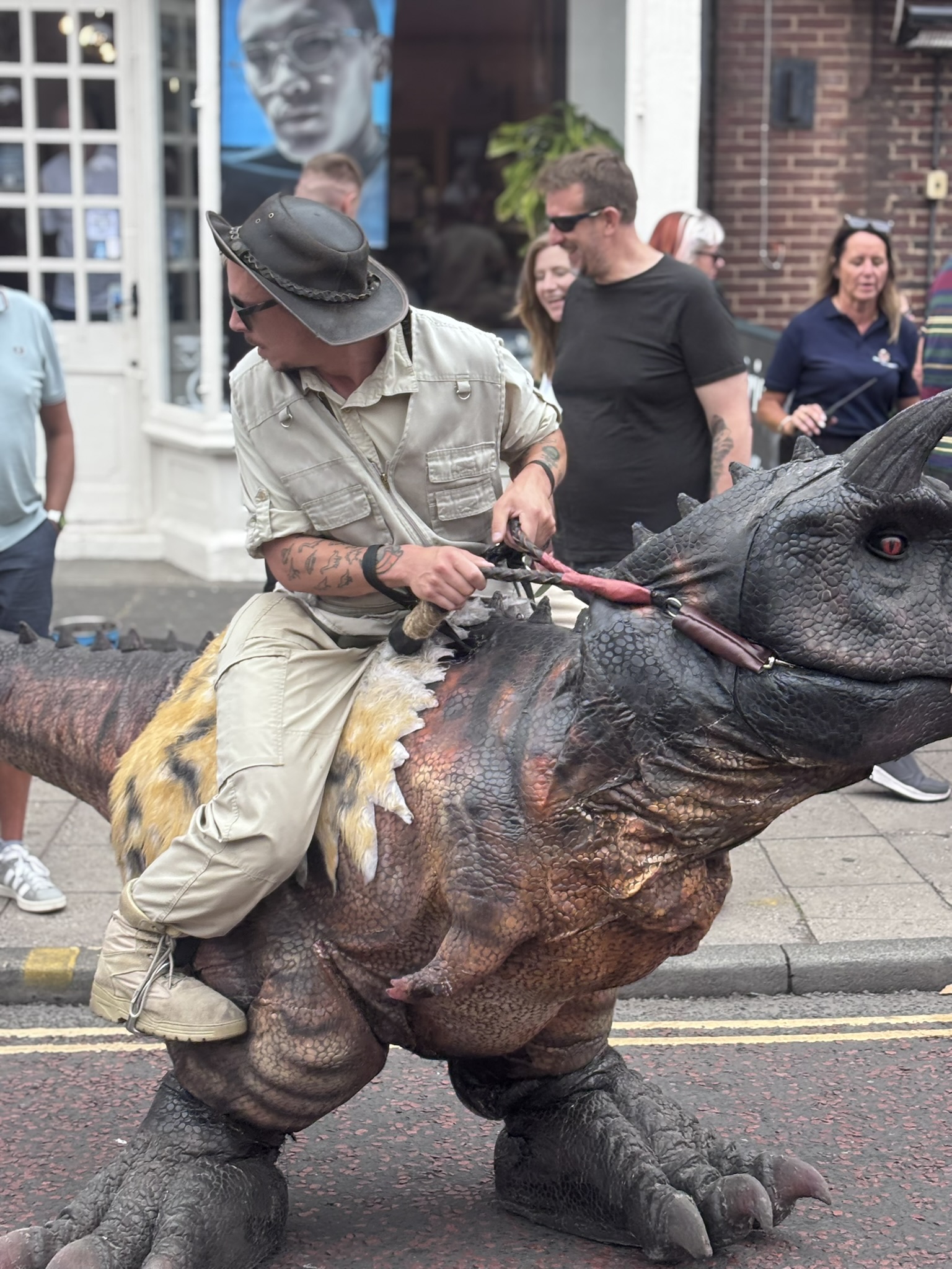 A man in a costume which makes it appear as so he's riding a dinosaur