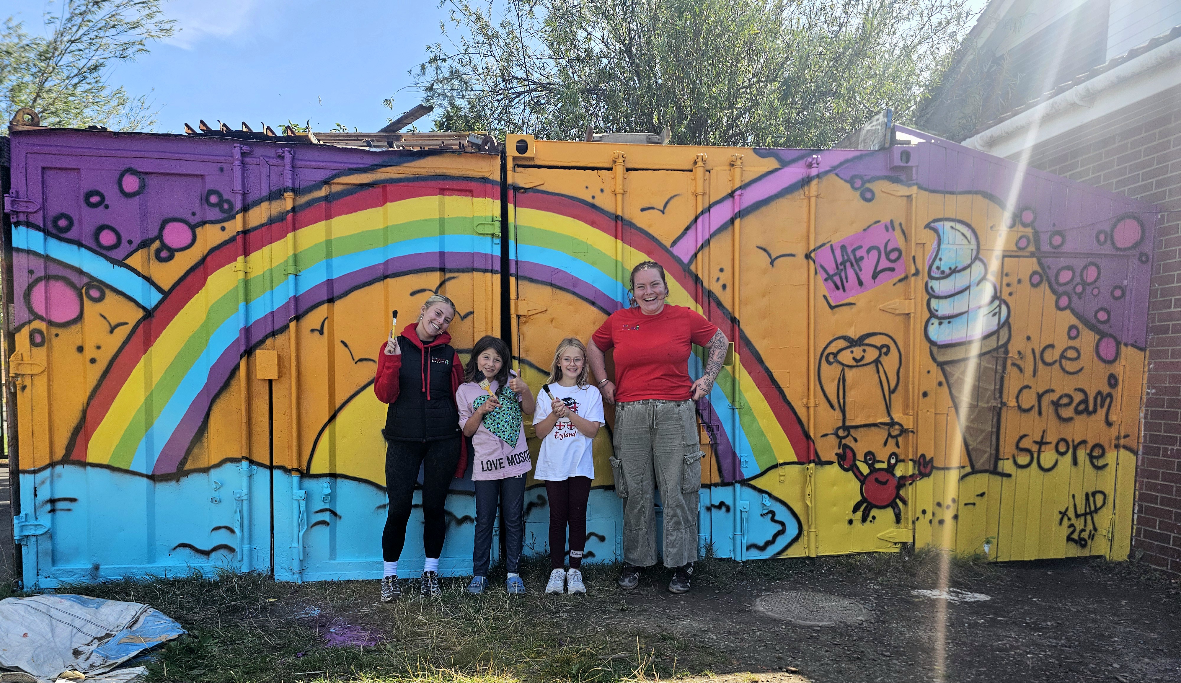 Two women and two children standing in front of a brightly coloured wall 