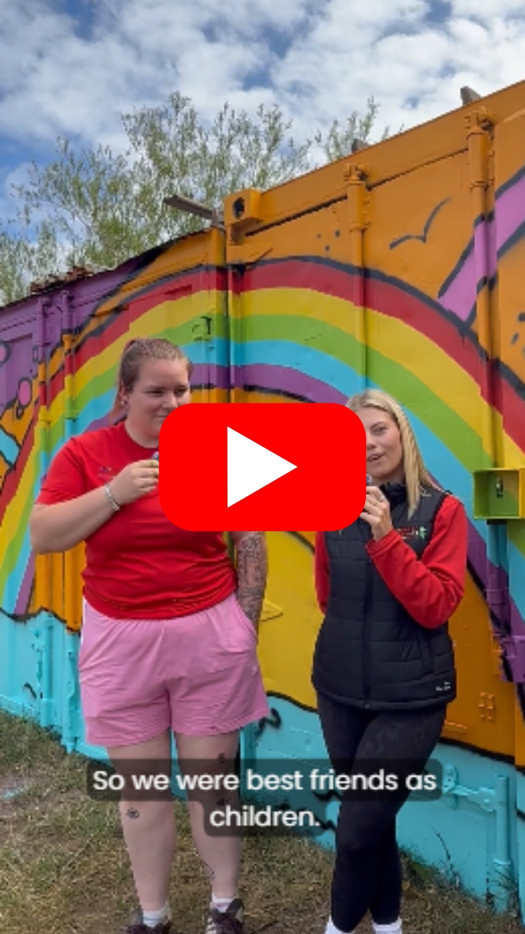 Two women standing in front of a brightly coloured mural