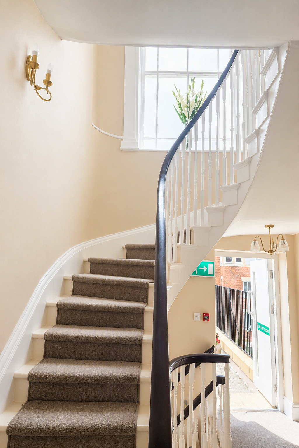 A staircase under a large window with a vase of flowers