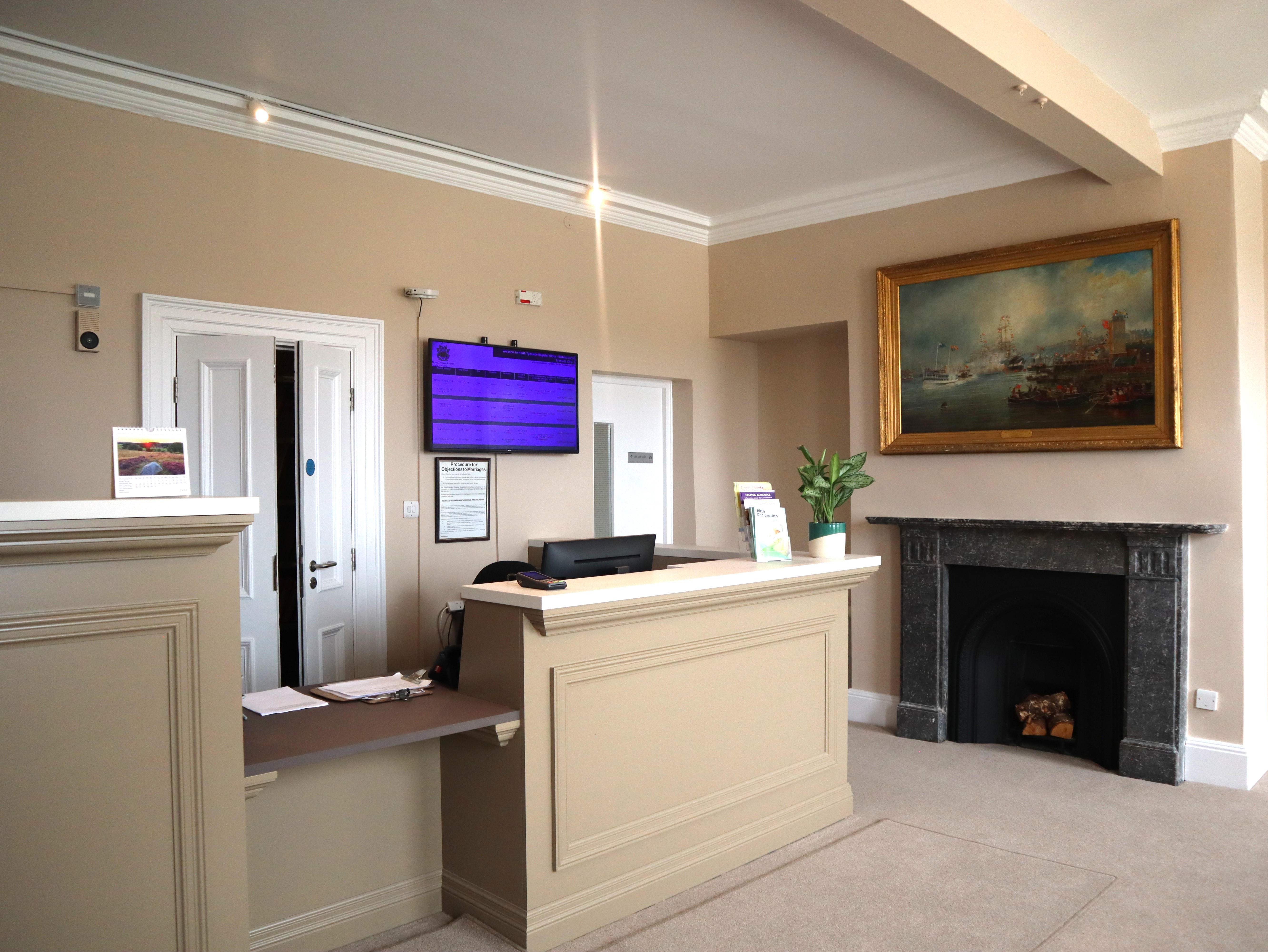 A reception room with a light coloured desk and fireplace