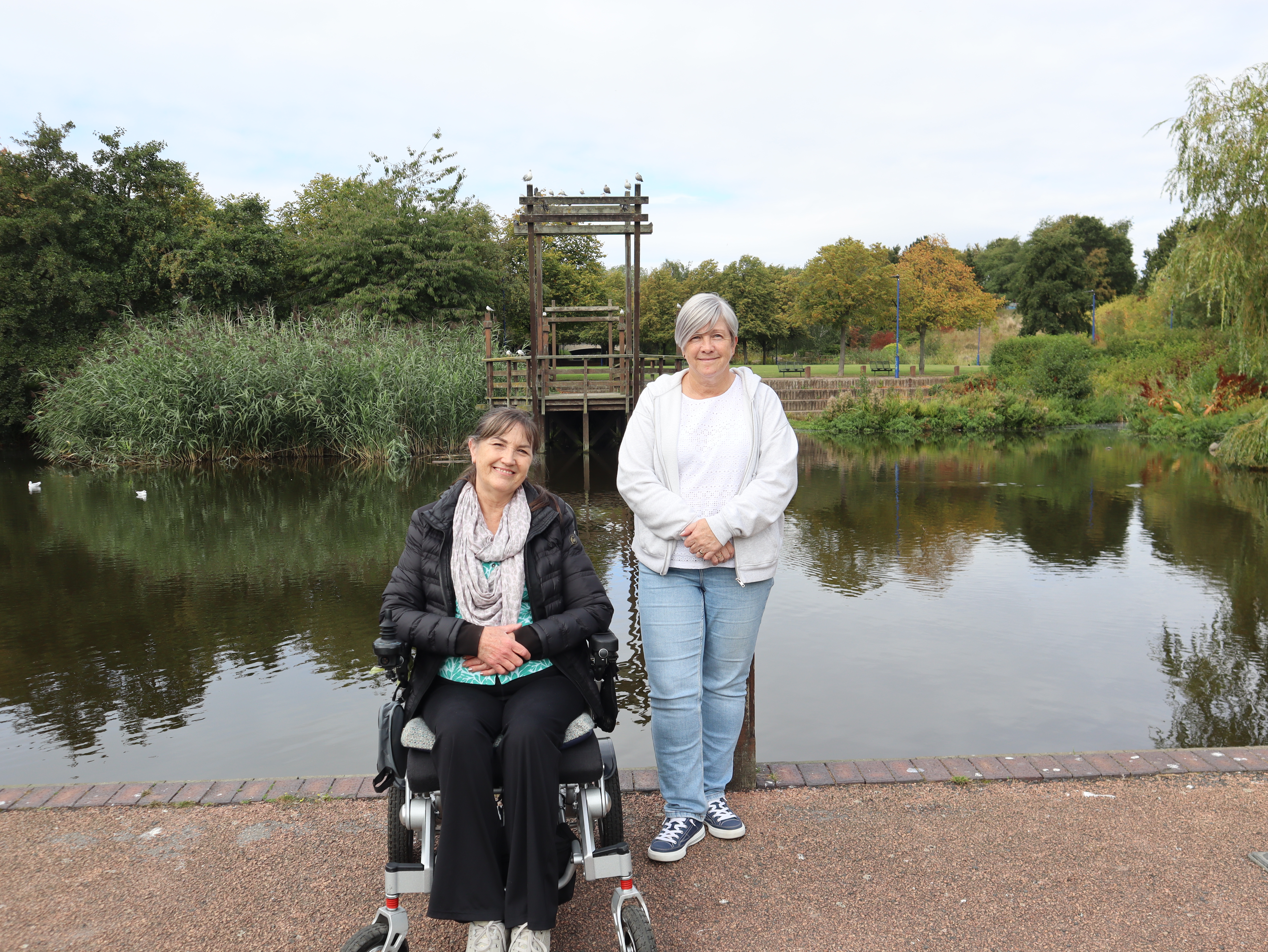 Two female volunteers pictured at the centre of Chirton Dene park in front of the lake 