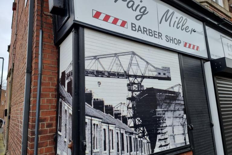 A colour photo of a barber shop with a vinyl of a black and white photo covering its shutters