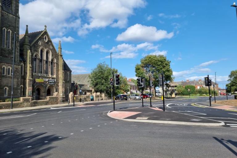 An image of the Stephenson Street gateway showing the road junction, cycle lane and crossing with a church and trees