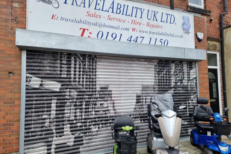 A colour photo of a mobility scooter shop with a vinyl of a black and white photo covering its shutters