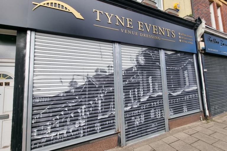 A colour photo of an events shop with a vinyl of a black and white photo covering its shutters