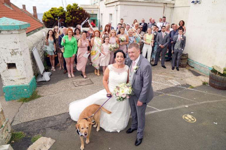 Guests with bride groom and dog outside lighthouse