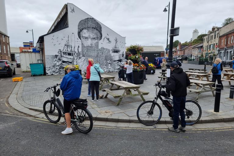 A group of visitors admire the Net Worth mural on North Shields Fish Quay including some cyclists and people on foot