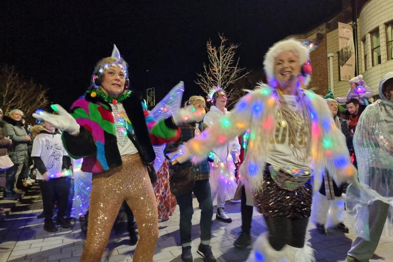 Women dancing dressed as illuminated fairies and smiling as part of a parade procession in a busy street at night