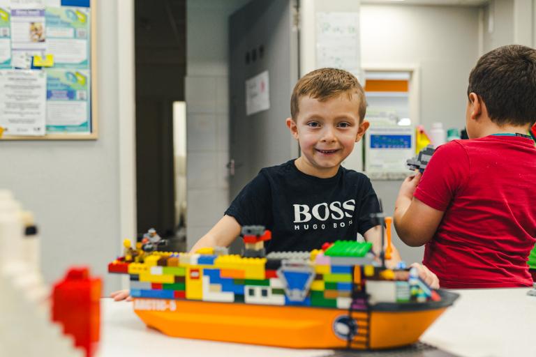 boy wearing a black t shirt building a boat out of lego blocks