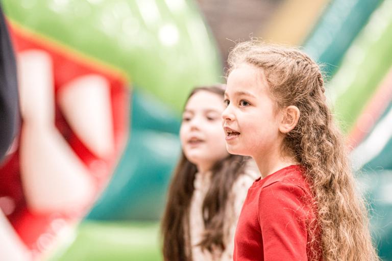 Two girls looking off to the left with a green and red bouncy castle in the background