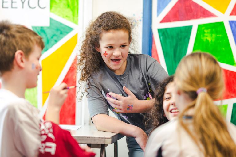 Children in a colourful room painting each other's faces