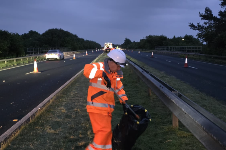 A man in a hi vis uniform litter picking on the verges of the A19