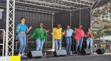 Group of six singers in colourful shirts singing and dancing on stage