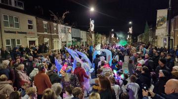 A crowded street with a carnival procession in North Shields town centre, it is dark and people are in costumes with some lit up with LEDs