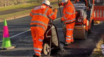 Two people in high-vis clothing laying bitumen onto the road