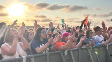 Cheering Crowds in front of the stage, with a beautiful sunset in the back round.