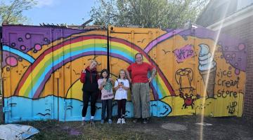 Two women and two children standing in front of a brightly coloured wall 