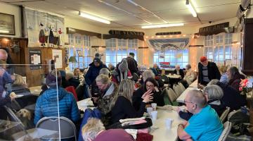 People in community hub sitting round tables with hot drinks
