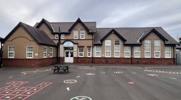 An exterior view of Forest Hall Primary School with a playground in the foreground it is a two storey building with lots of windows 