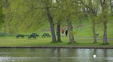 Lake surrounded by trees with two people walking along the path. 