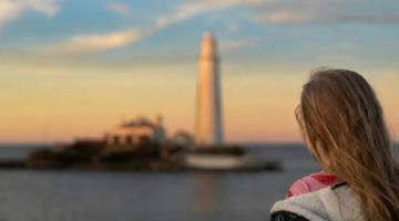 Young girl pictured looking at a Sunset over St Mary's Lighthouse causeway
