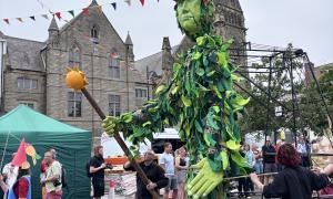 An enormous, green puppet, wanders through the streets of Tynemouth, staff in hand as part of the parade, pre-concert