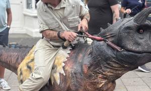 A man in a costume which makes it appear as so he's riding a dinosaur