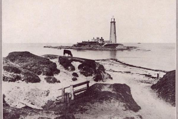 A black and white photograph of the coast with a lighthouse in the background
