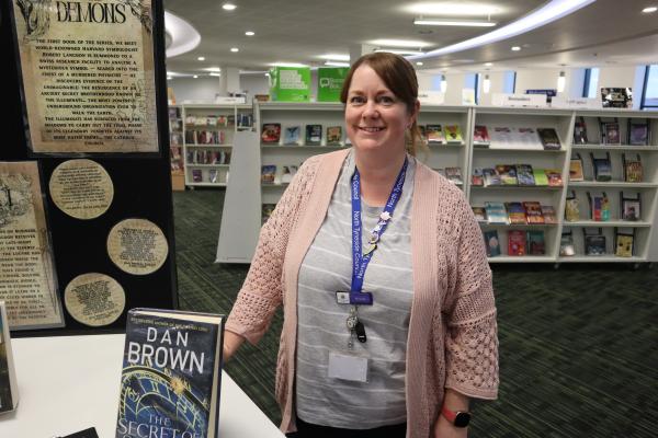 Smiling person wearing a badge. They're in the library
