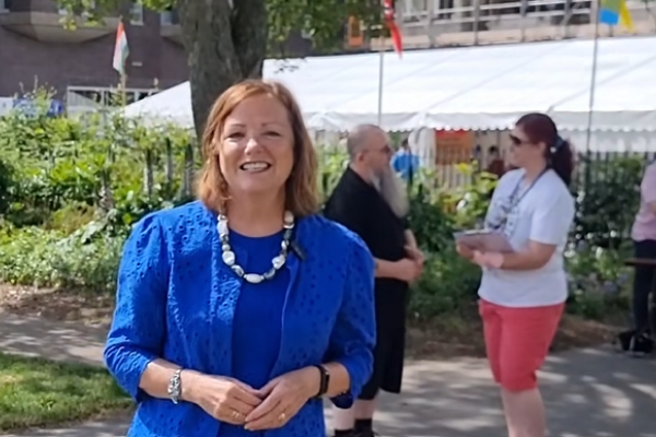 Elected Mayor in blue dress and gold necklace standing in front of a festival marquee