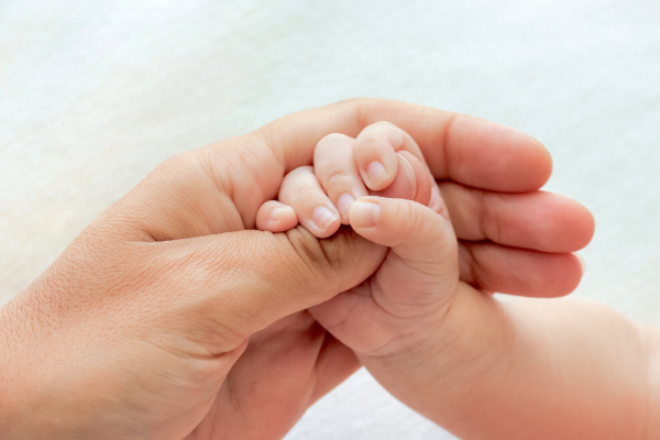 An adult hand holding a babies hand
