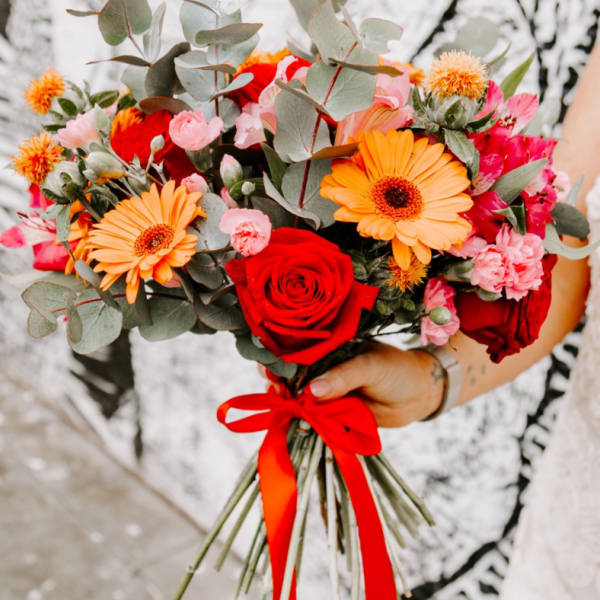 A bouquet of red, orange and pink flowers tied up with a red ribbon