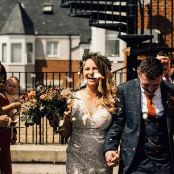 A smiling couple of their wedding daywalking out of the ceremony holding hands, confetti is thrown over them. 